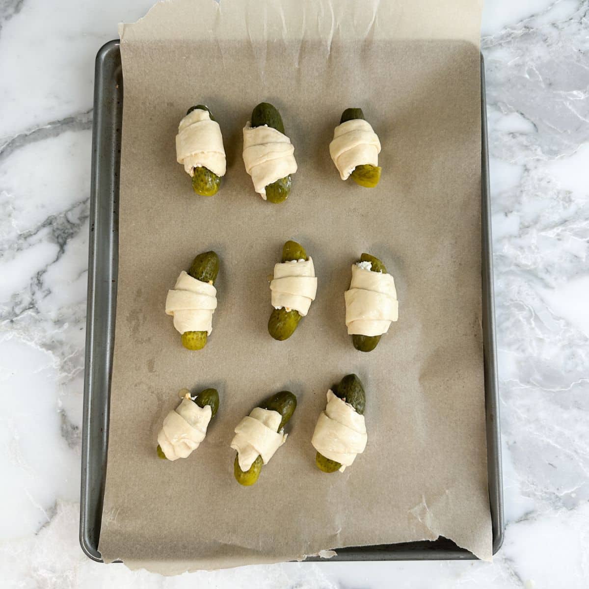 Baking pan with unbaked pickles in a blanket. 