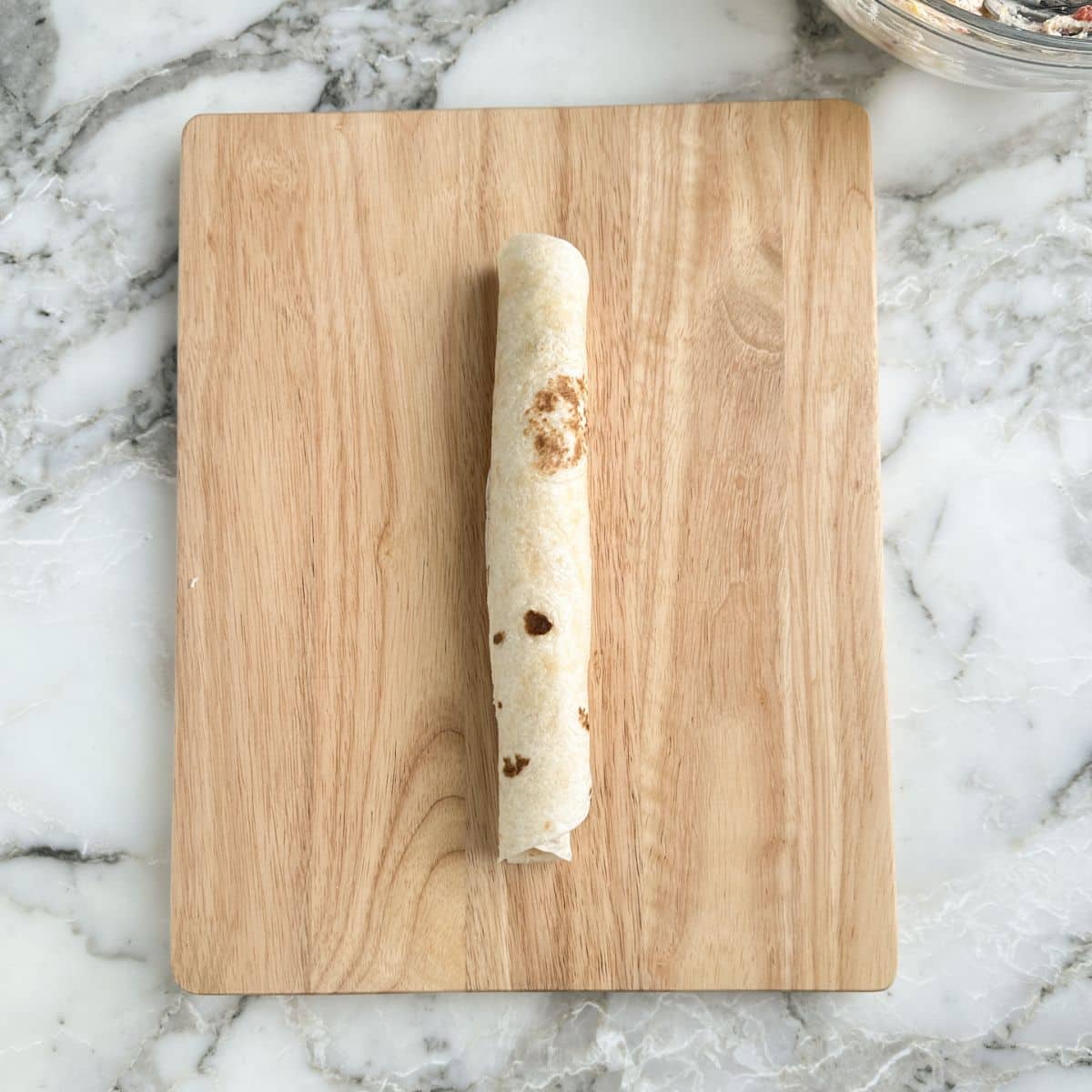 Rolled up tortilla on a wooden cutting board. 