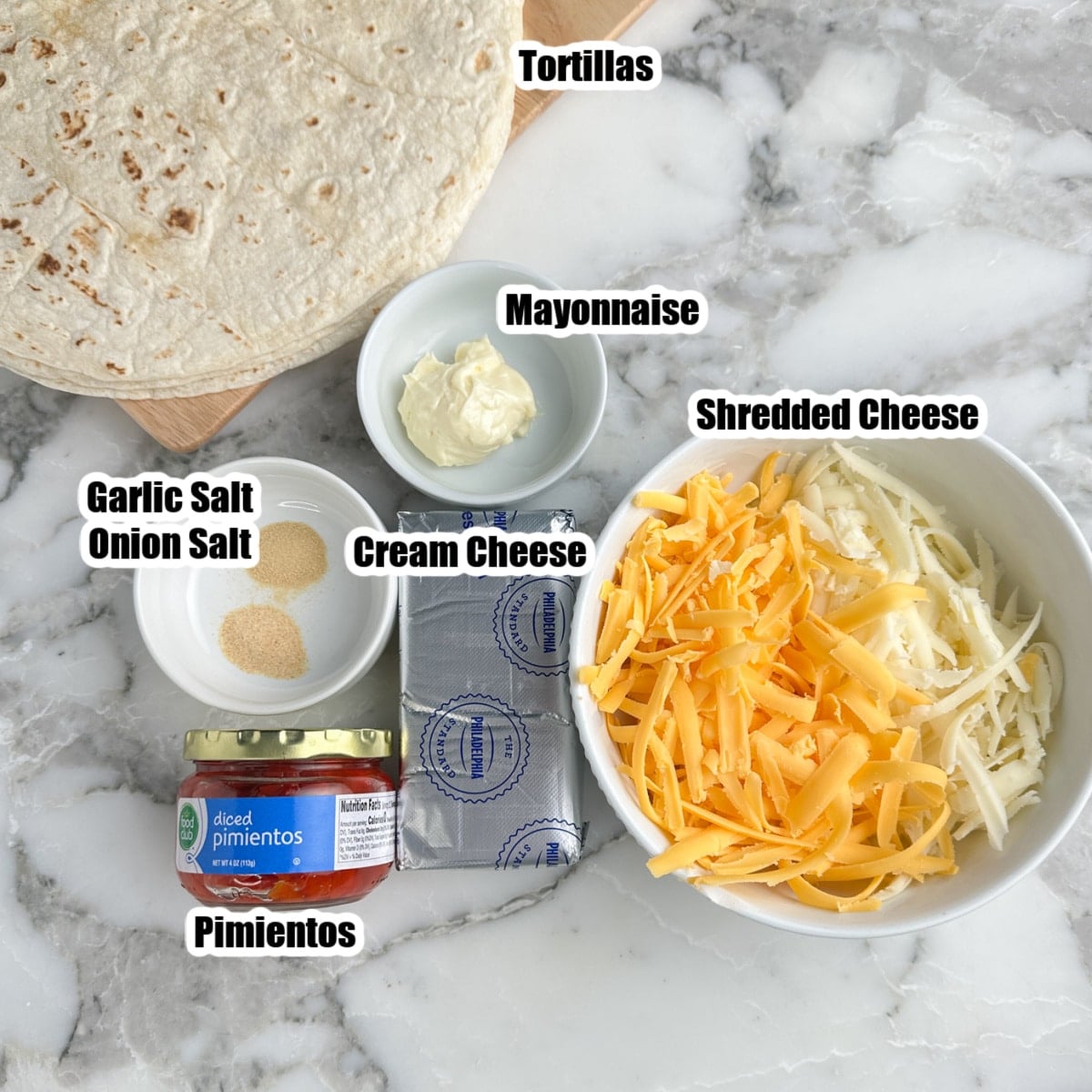 Bowl of shredded cheese, jar of pimentos, cream cheese, mayonnaise, tortillas, garlic powder, onion powder. 