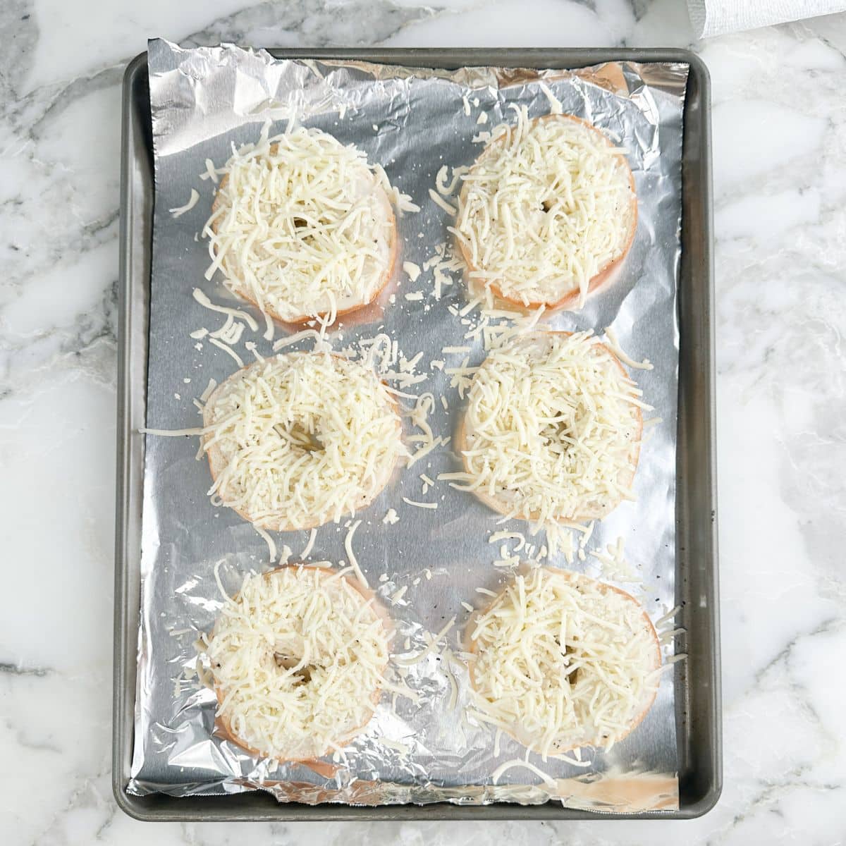 Baking paan with bagels topped with gravy and shredded cheese.