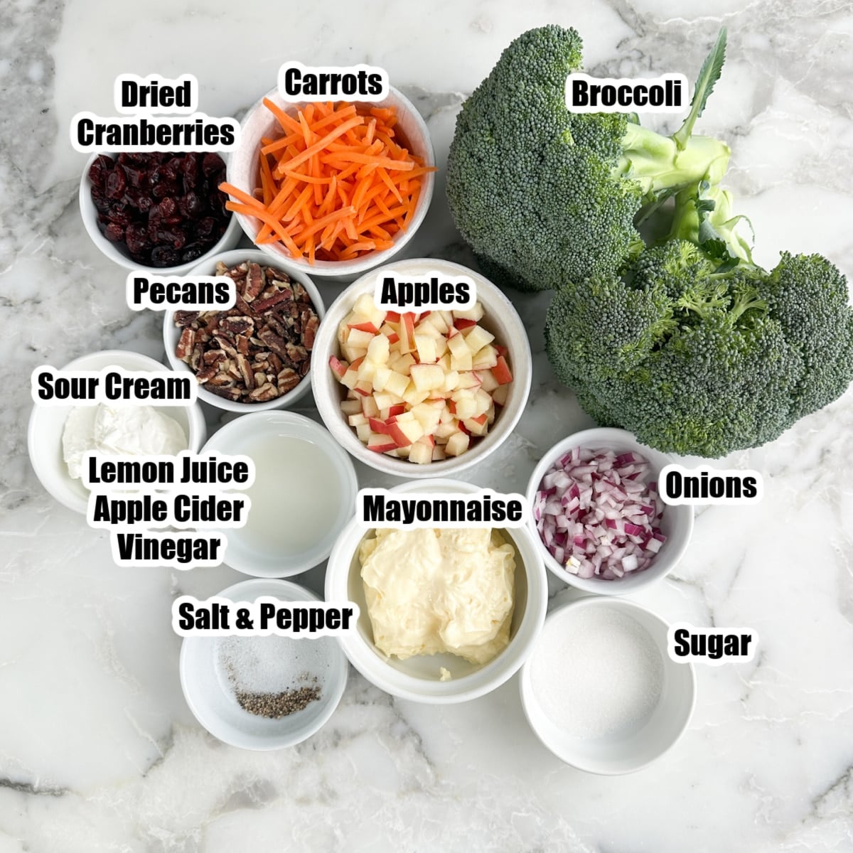 Broccoli, shredded carrots, diced apples, onions, mayonnaise, cranberries, pecans, sour cream, sugar, salt, and pepper.