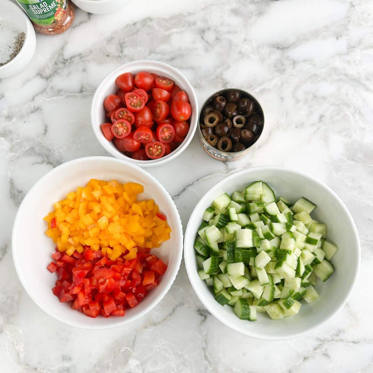 Bowl of diced cucumber, diced bell peppers, tomatoes, and sliced olives. 