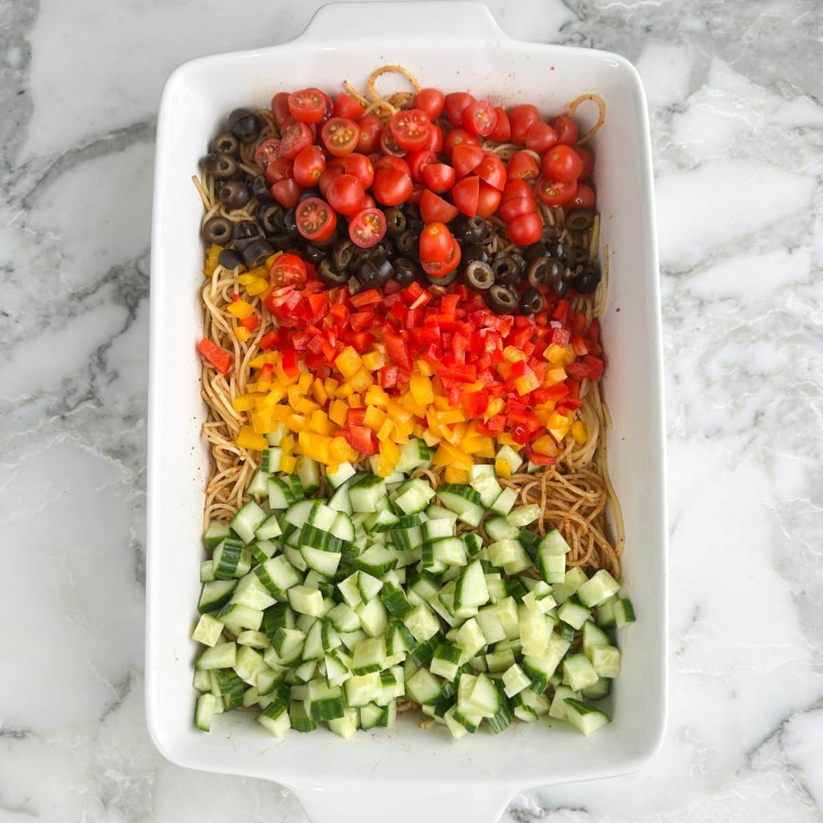 Casserole dish with diced cucumbers, diced peppers, olives, and tomatoes. 