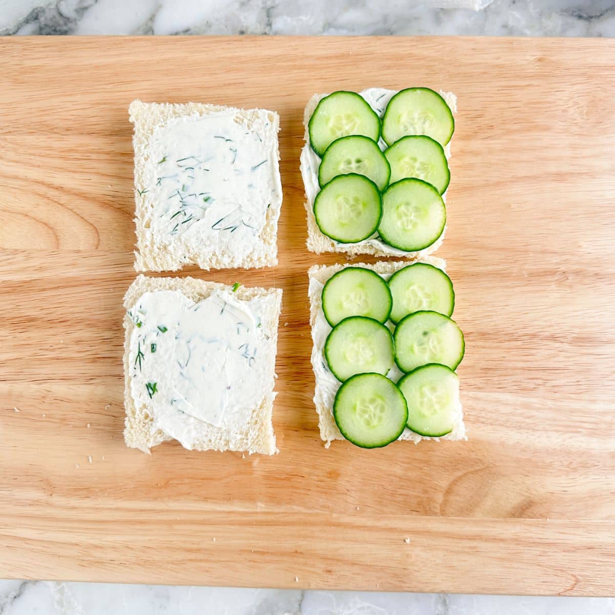 Pieces of bread spread with cream cheese and sliced cucumbers.