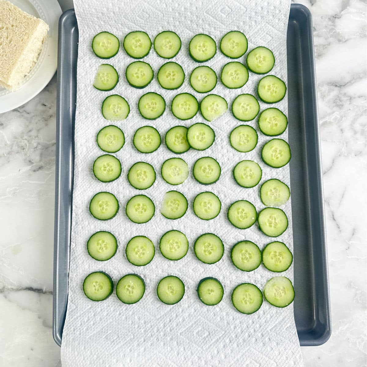 Baking pan with a paper towel and sliced cucumbers.