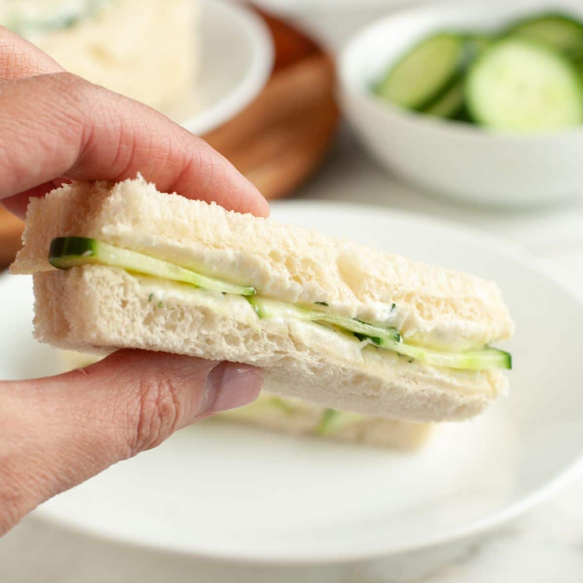 Hand holding cucumber sandwich.