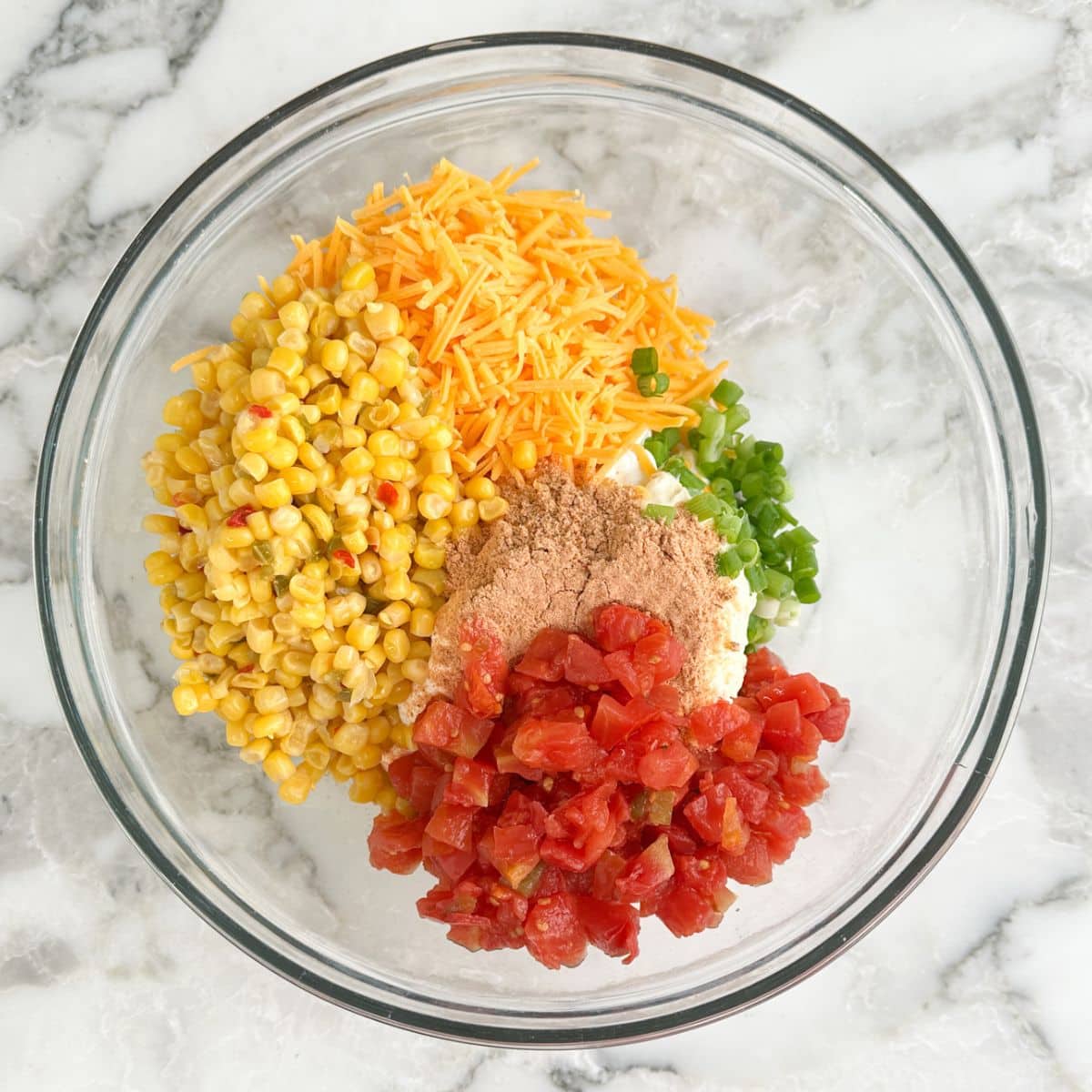 Bowl with corn kernels, diced tomatoes, shredded cheese, seasonings, green onion, and sour cream. 