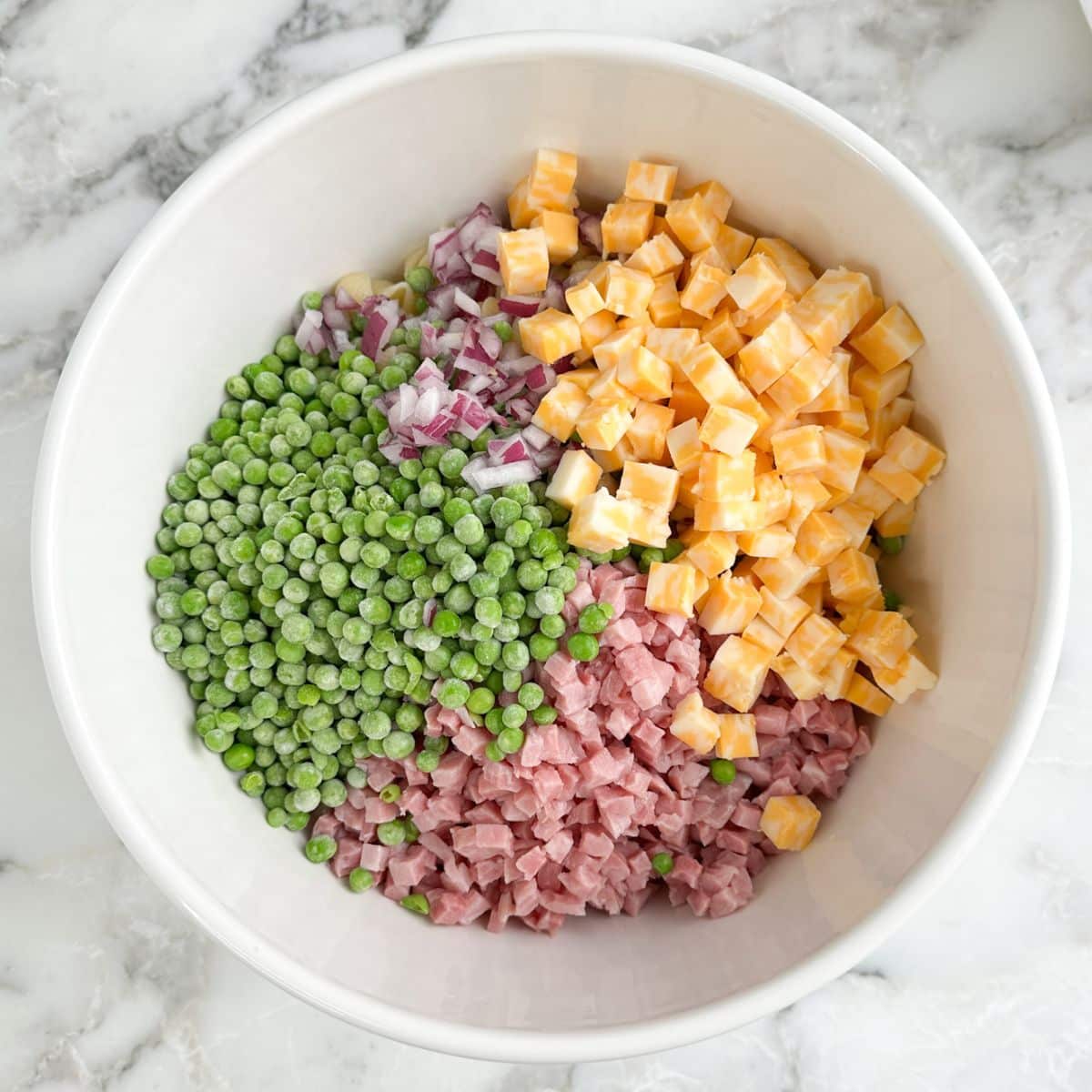 Bowl of peas, cubed cheese, diced ham, and red onions. 
