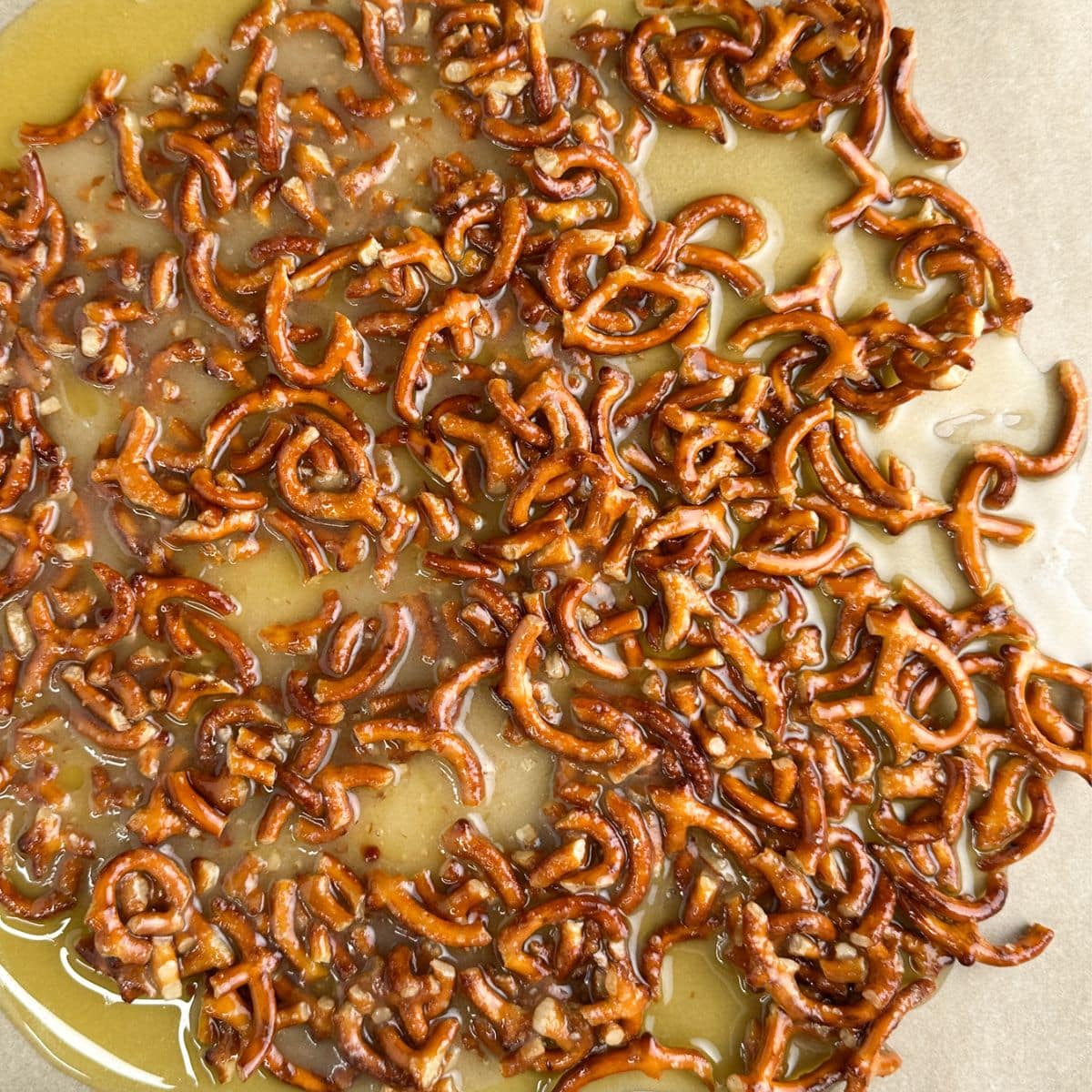 Broken pretzels in melted butter on a baking sheet. 