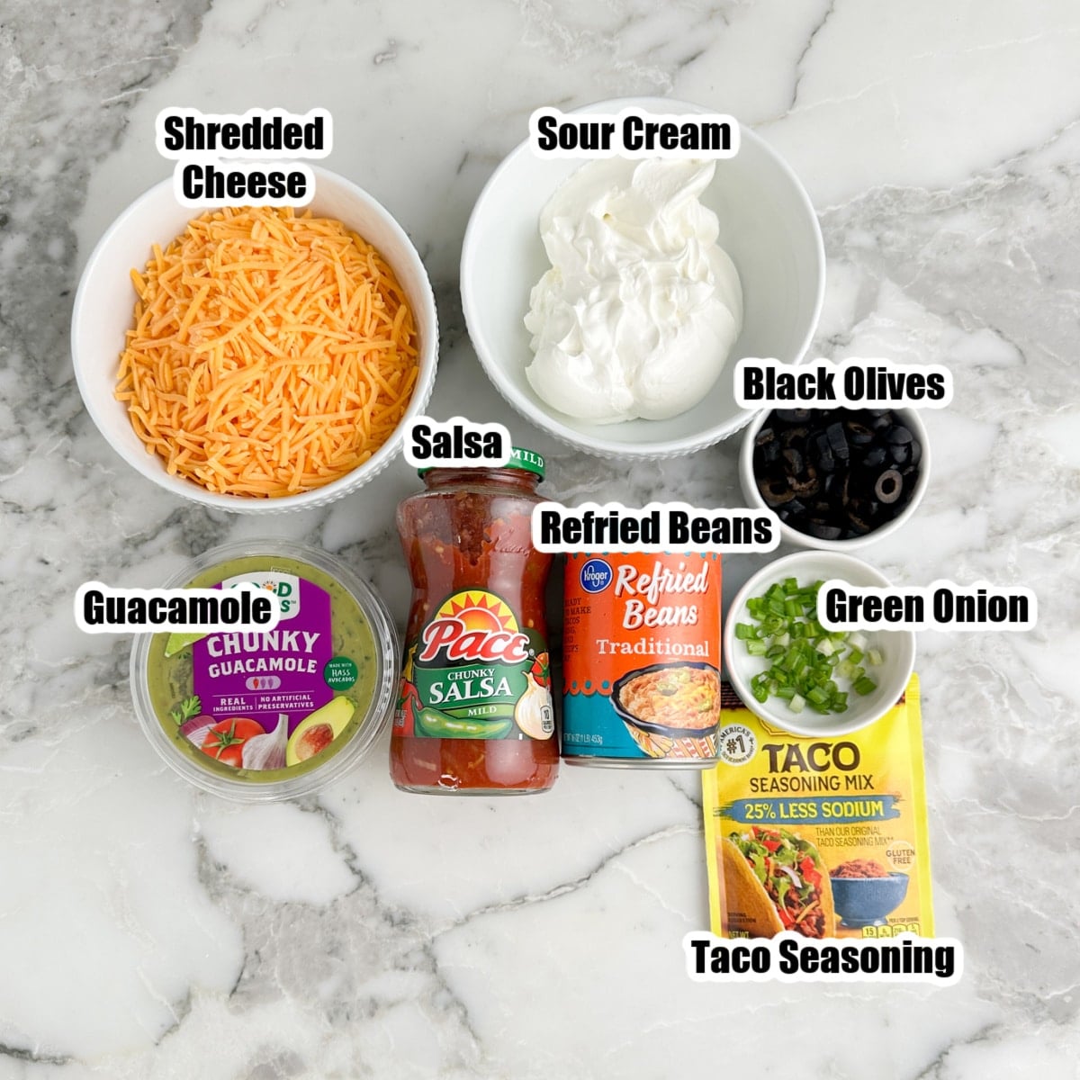 Bowl of shredded cheese, sour cream, salsa, guacamole, beans, taco seasonings, olives, and green onions.
