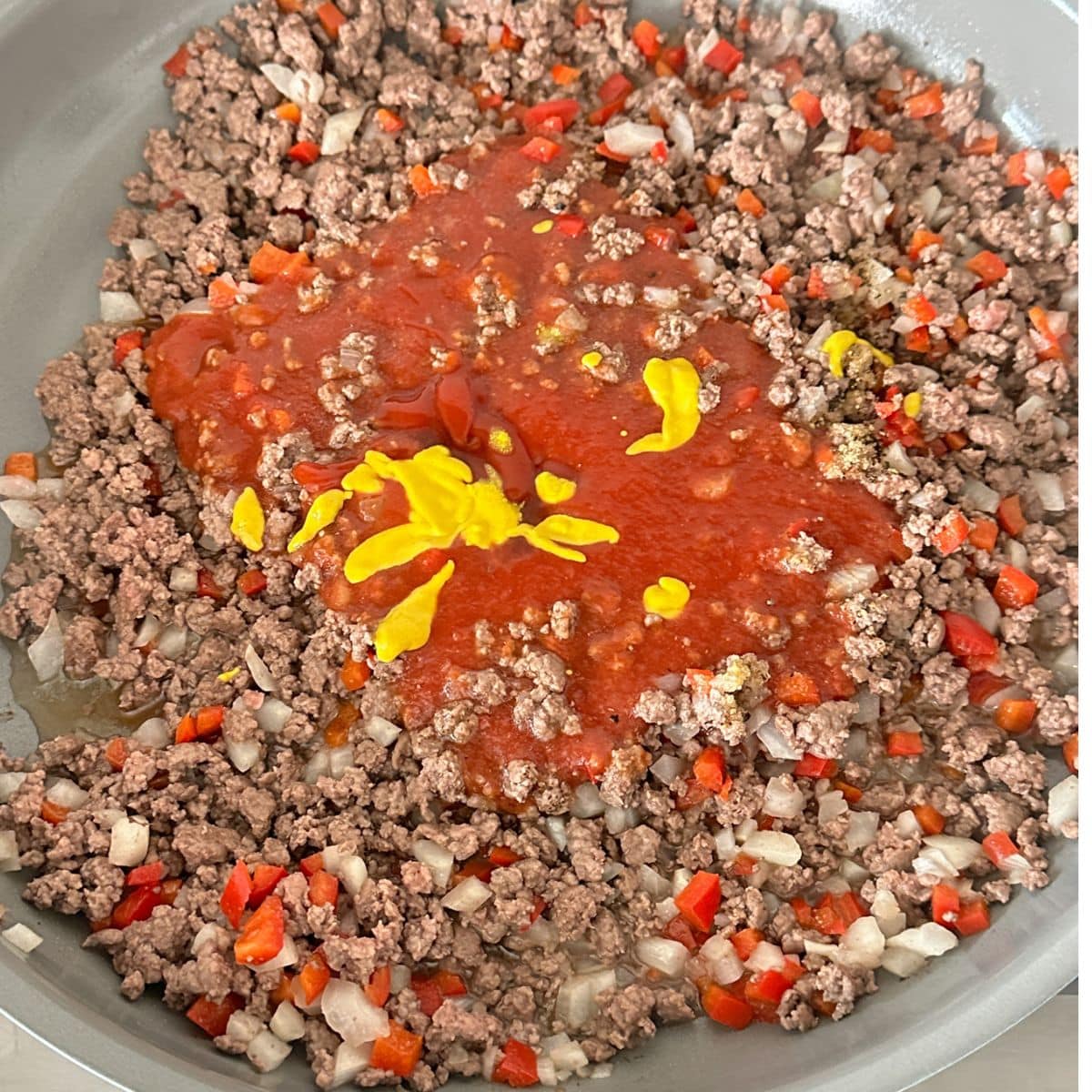 Skillet with ground beef, ketchup, mustard, and tomato sauce.