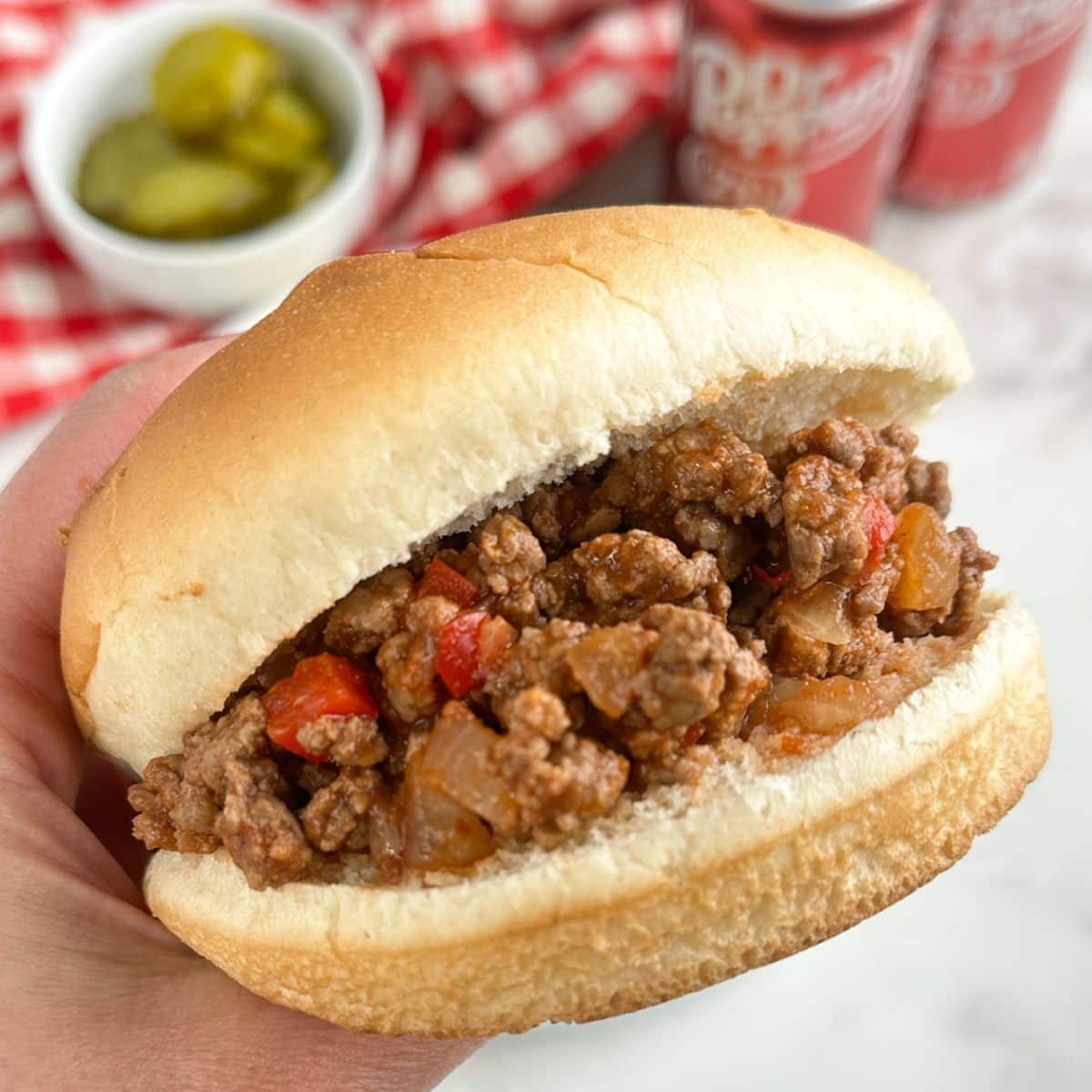 Hand holding a Dr. Pepper sloppy joe sandwich.