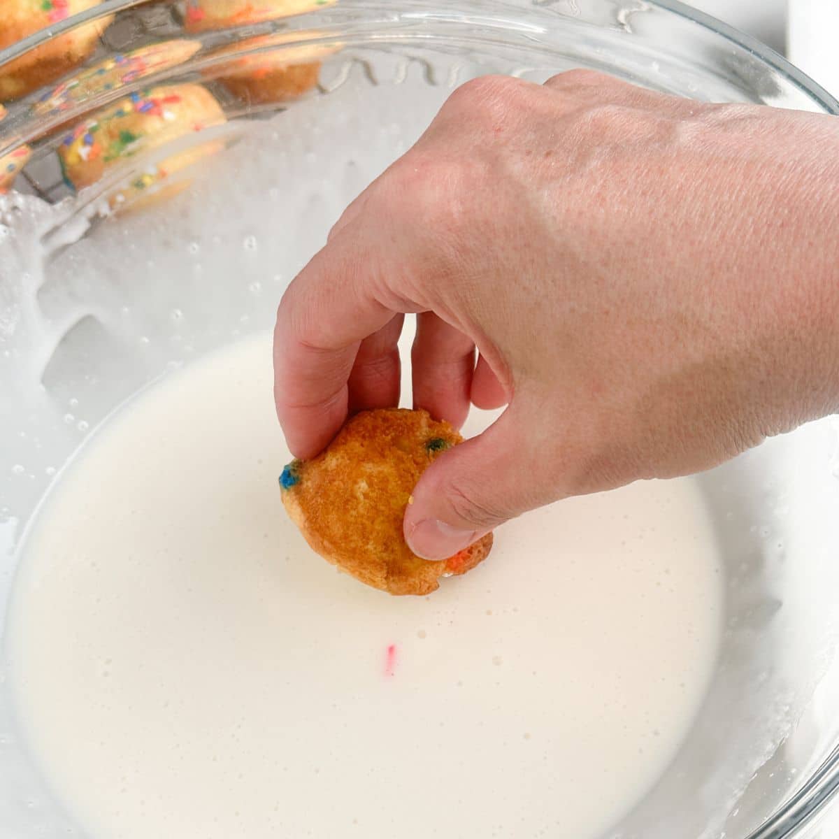Bowl of icing with mini cake being dipped in.
