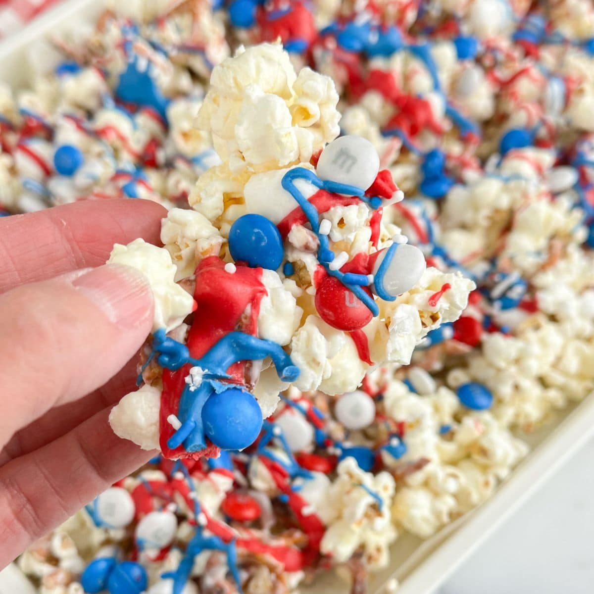 Hand holding red white and blue popcorn snack mix.