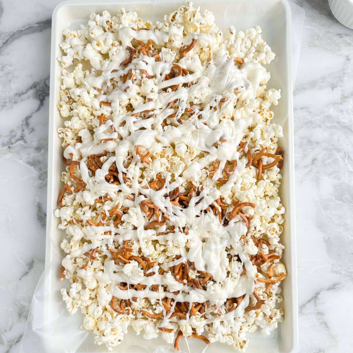 Baking sheet with popcorn, pretzels, mini marshmallows, and melted white chocolate.