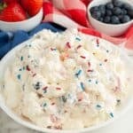 Bowl of red, white, and blue cheesecake salad with a bowl of strawberries and blueberries.