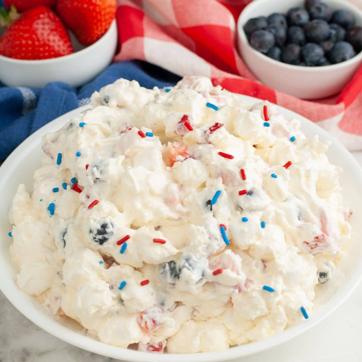  Bowl of red, white, and blue cheesecake salad with a bowl of strawberries and blueberries.