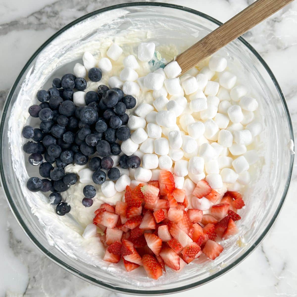 Bowl with cream cheese, mini marshmallows, blueberries, and strawberries. 