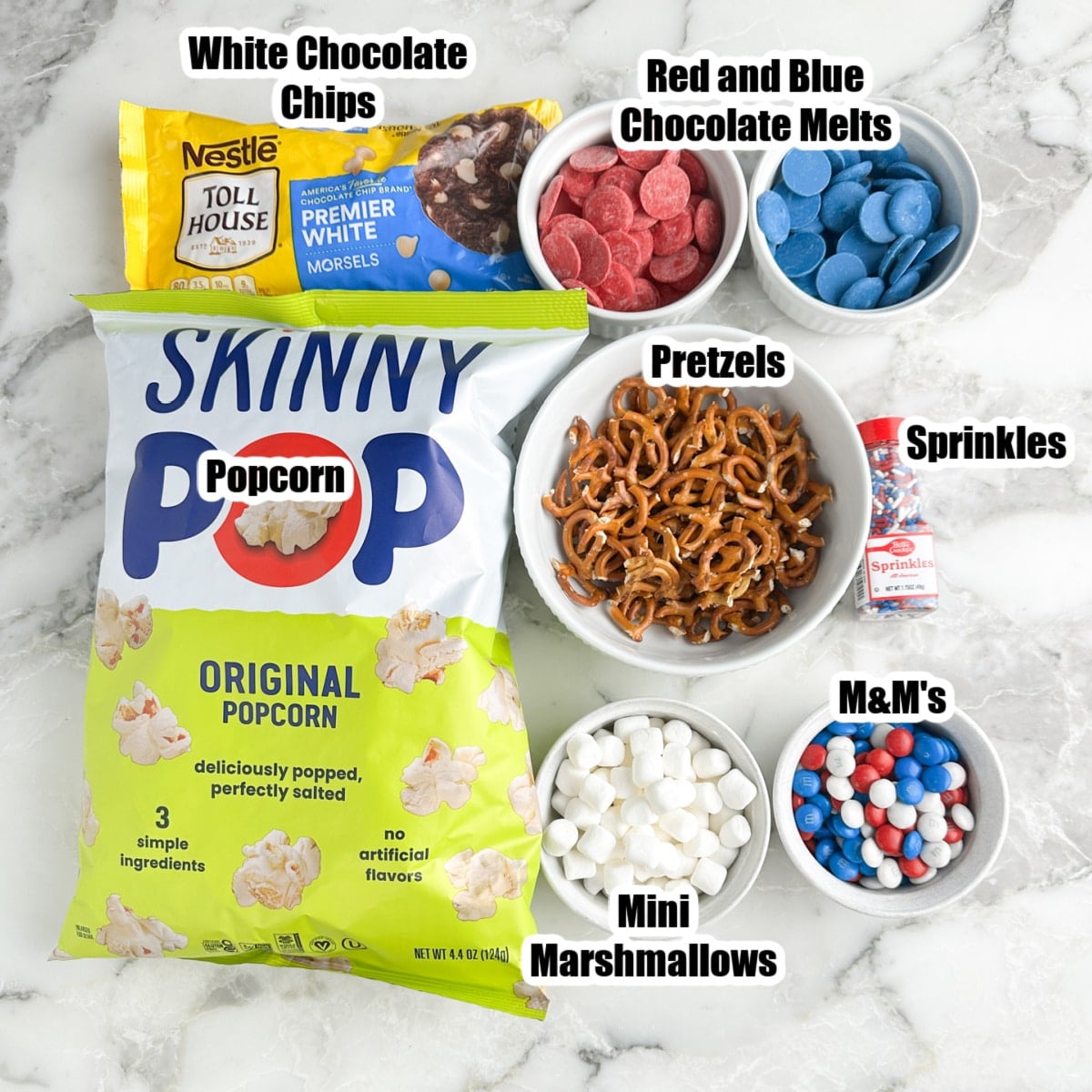 Bag of popcorn, bag of white chocolate chips, pretzels, sprinkles, mini marshmallows, candy, and red and blue chocolate melts.