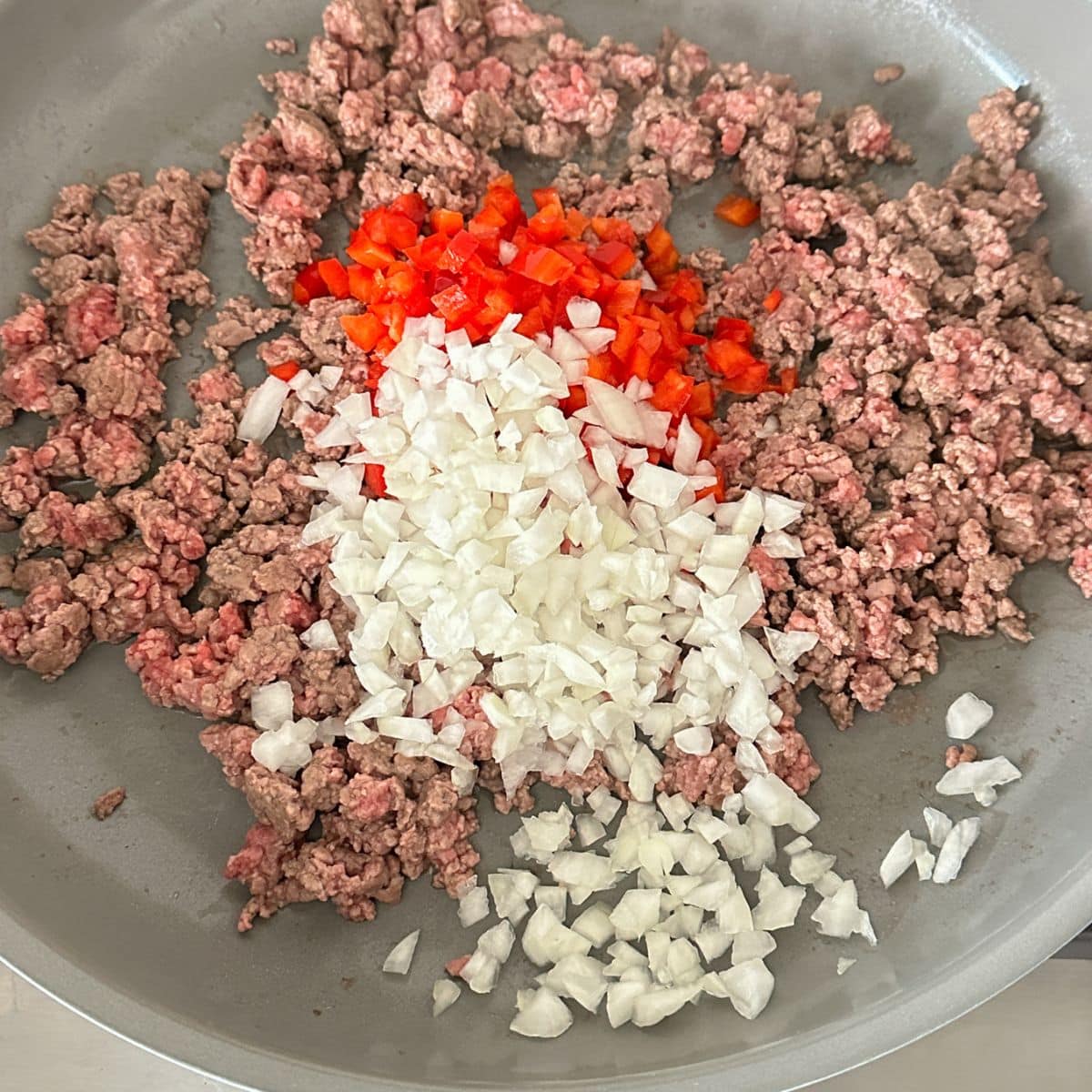 Skillet with ground beef, diced onions, and diced peppers.