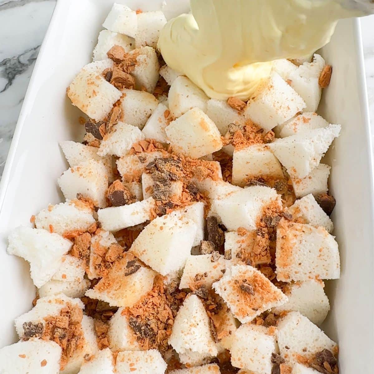 Cubed angel food cake and pudding in a casserole dish.