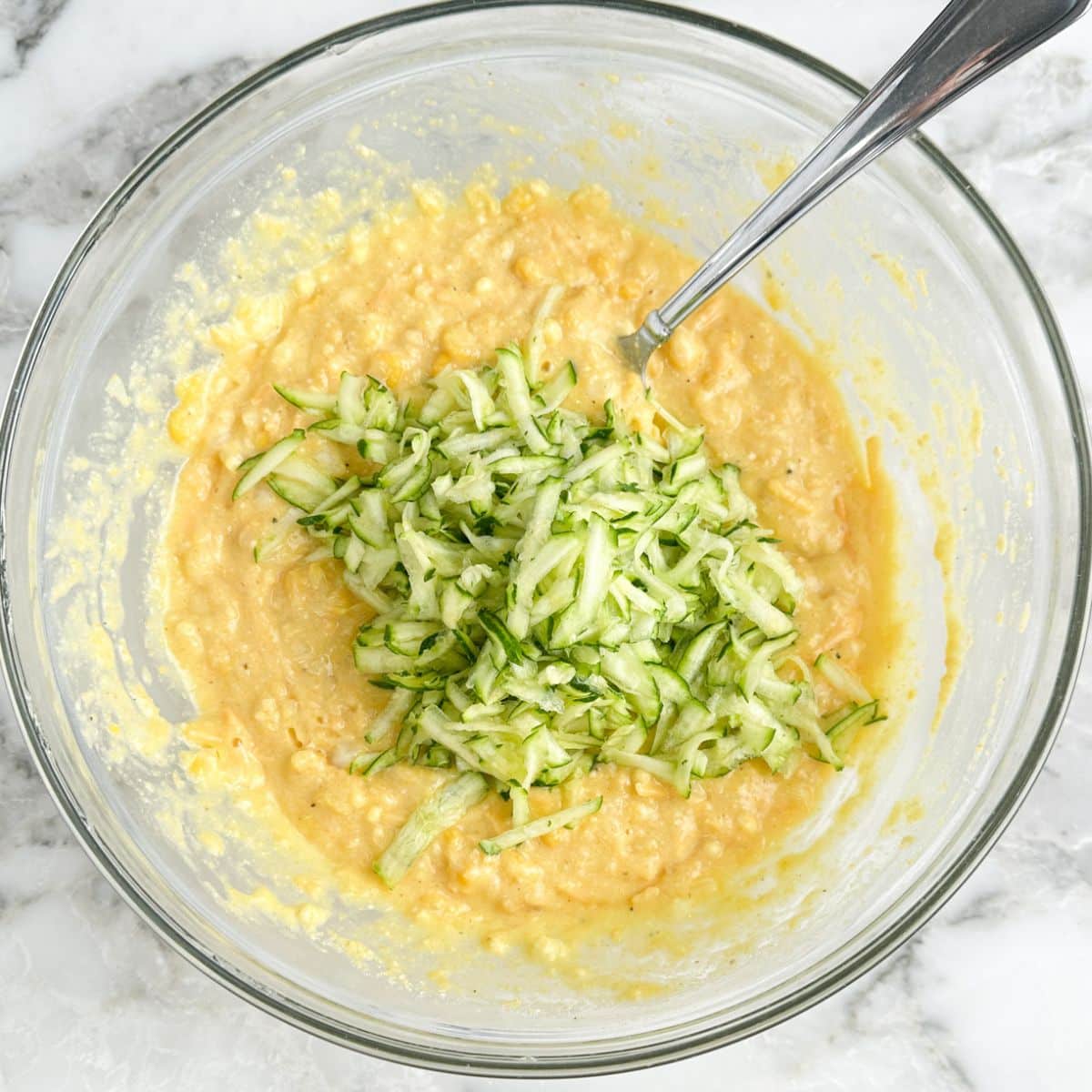 Bowl with cornbread batter and shredded zucchini. 