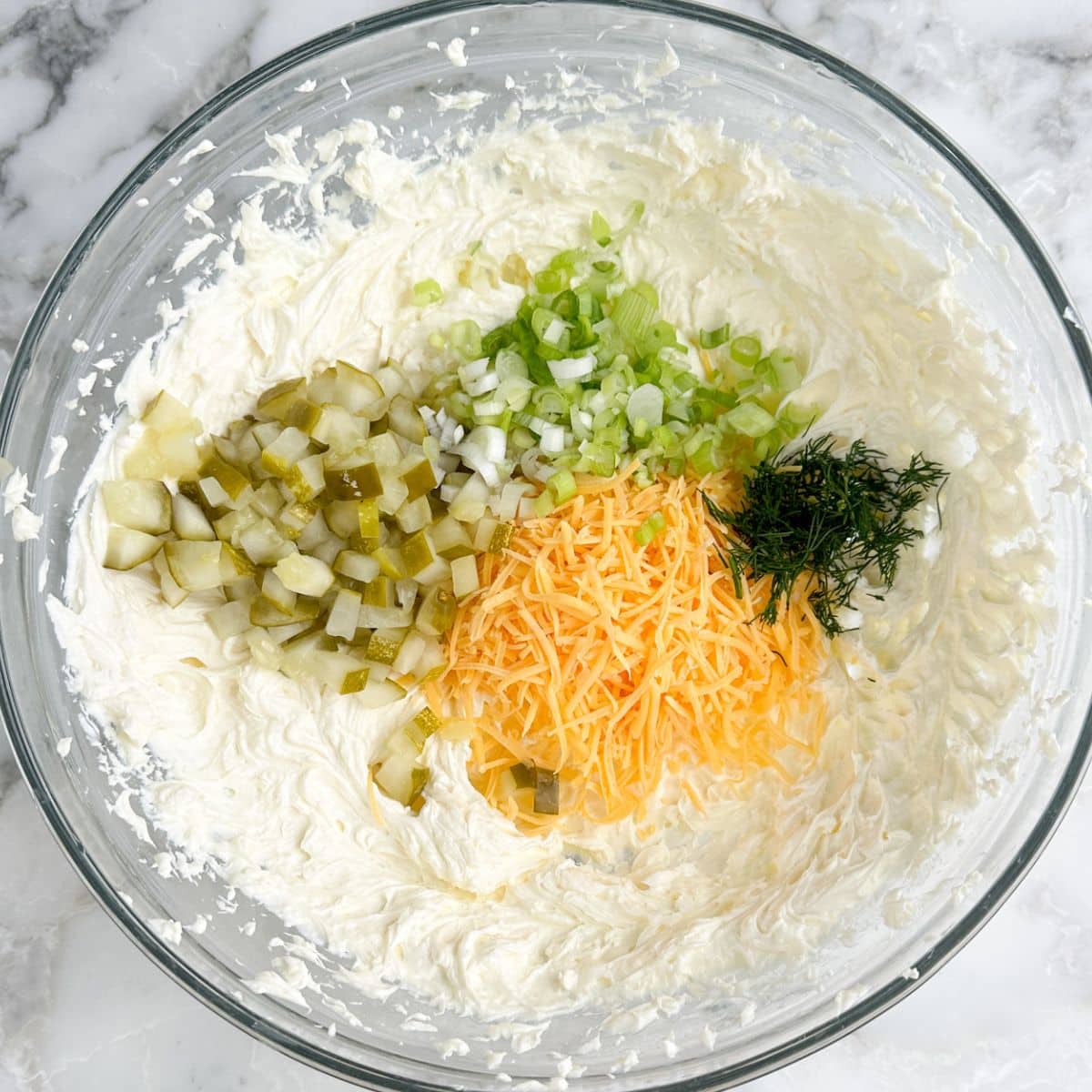 Bowl of cream cheese, diced pickles, shredded cheese, green onions.