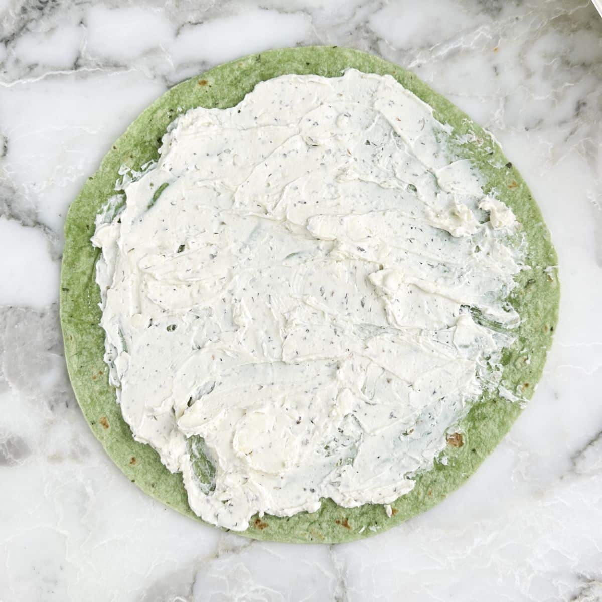 Green tortilla with cream cheese spread on top.