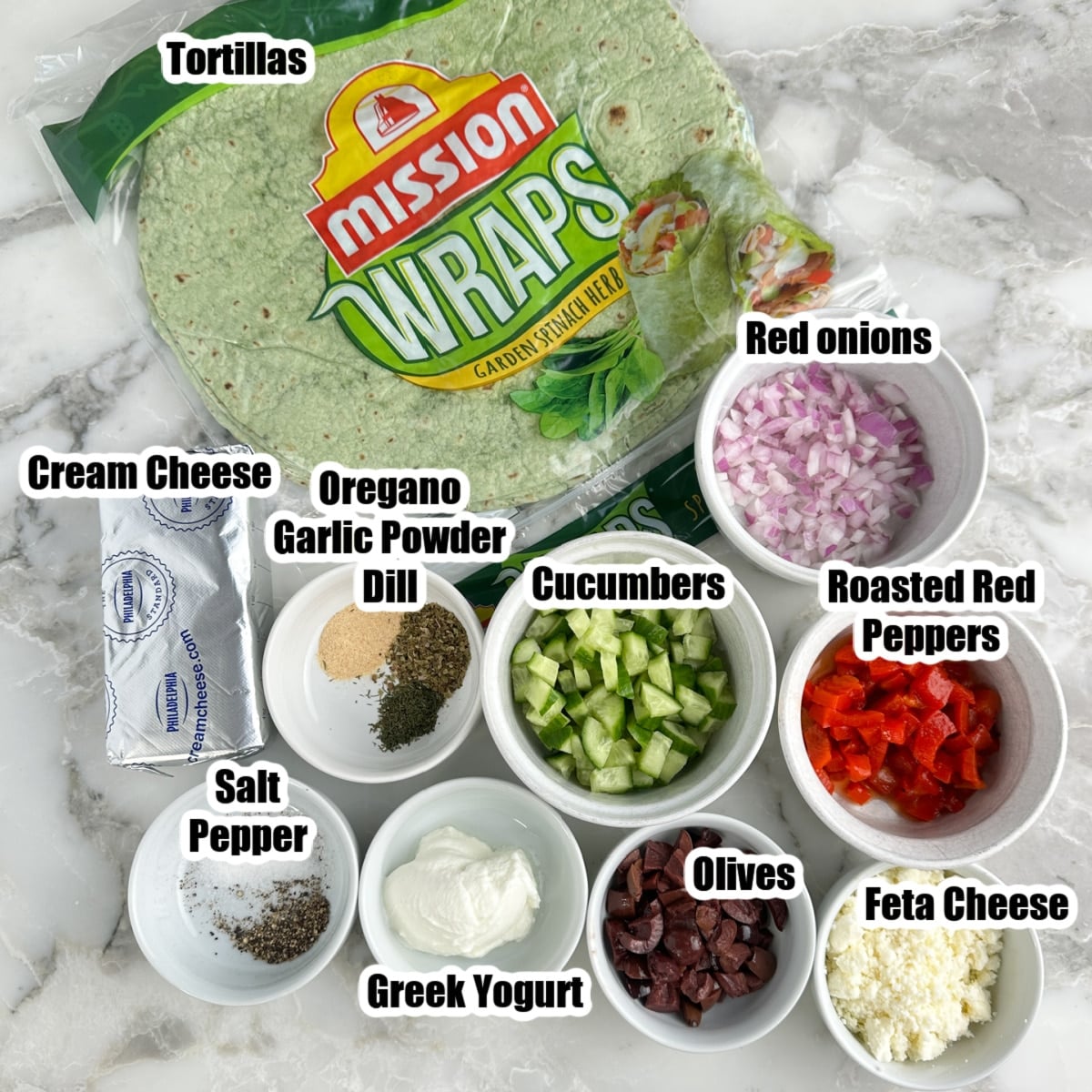 Spinach tortillas, bowls of red onions, cucumber, Greek yogurt, roasted red pepper, Feta cheese, olives, cream cheese, and seasonings.
