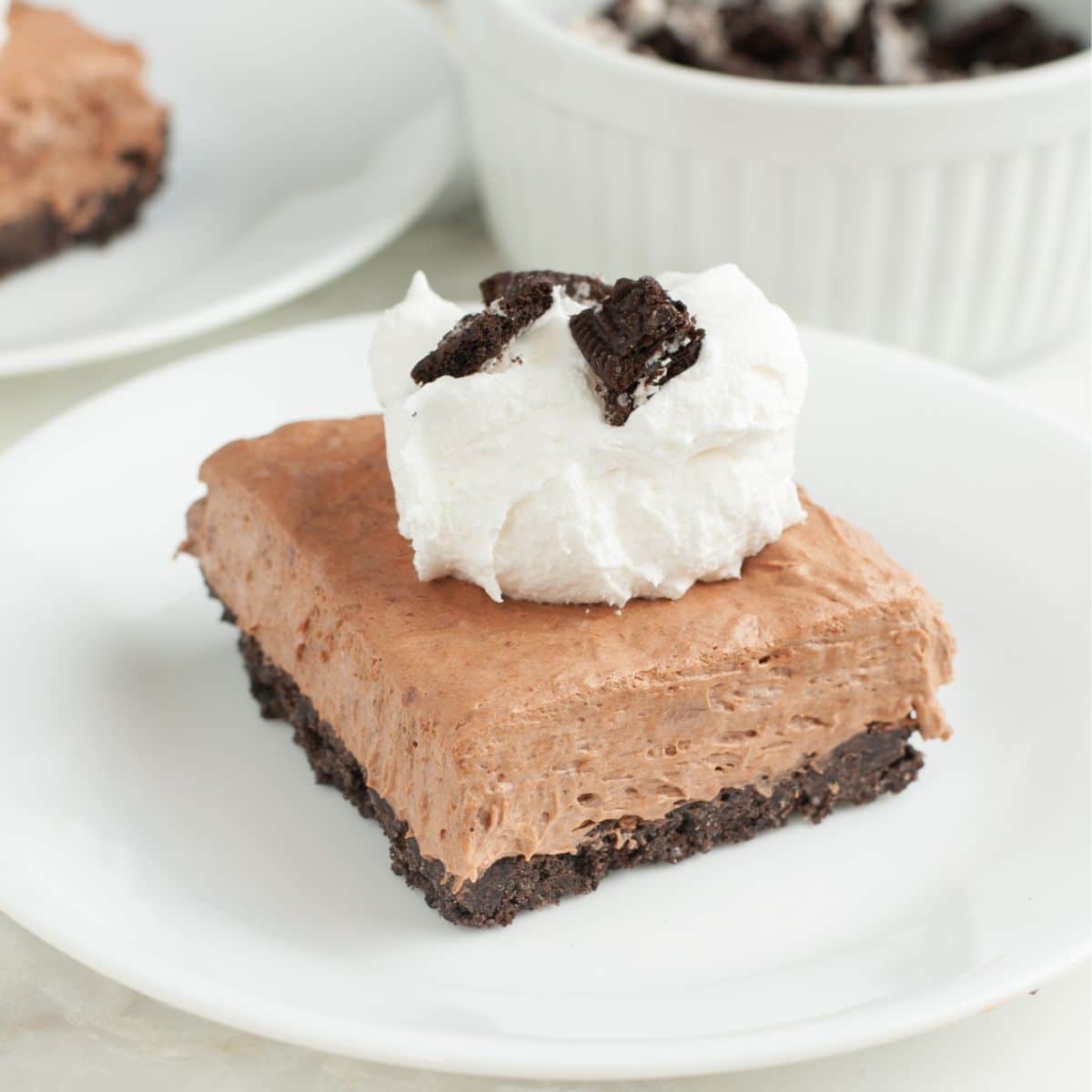Piece of no bake chocolate pie topped with whipped cream and crumbled Oreo cookies. 