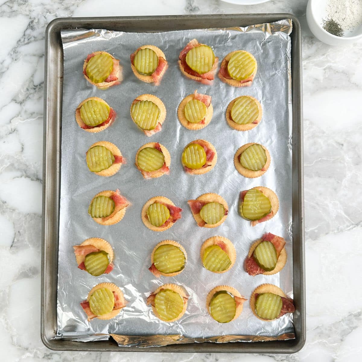 Crackers topped with bacon and dill pickle slices.