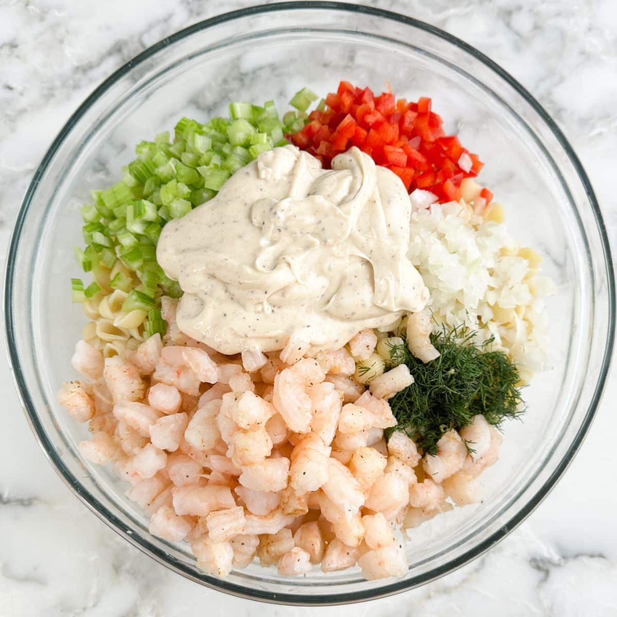 Bowl of pasta, cooked shrimp, celery, pepper, and dressing. 