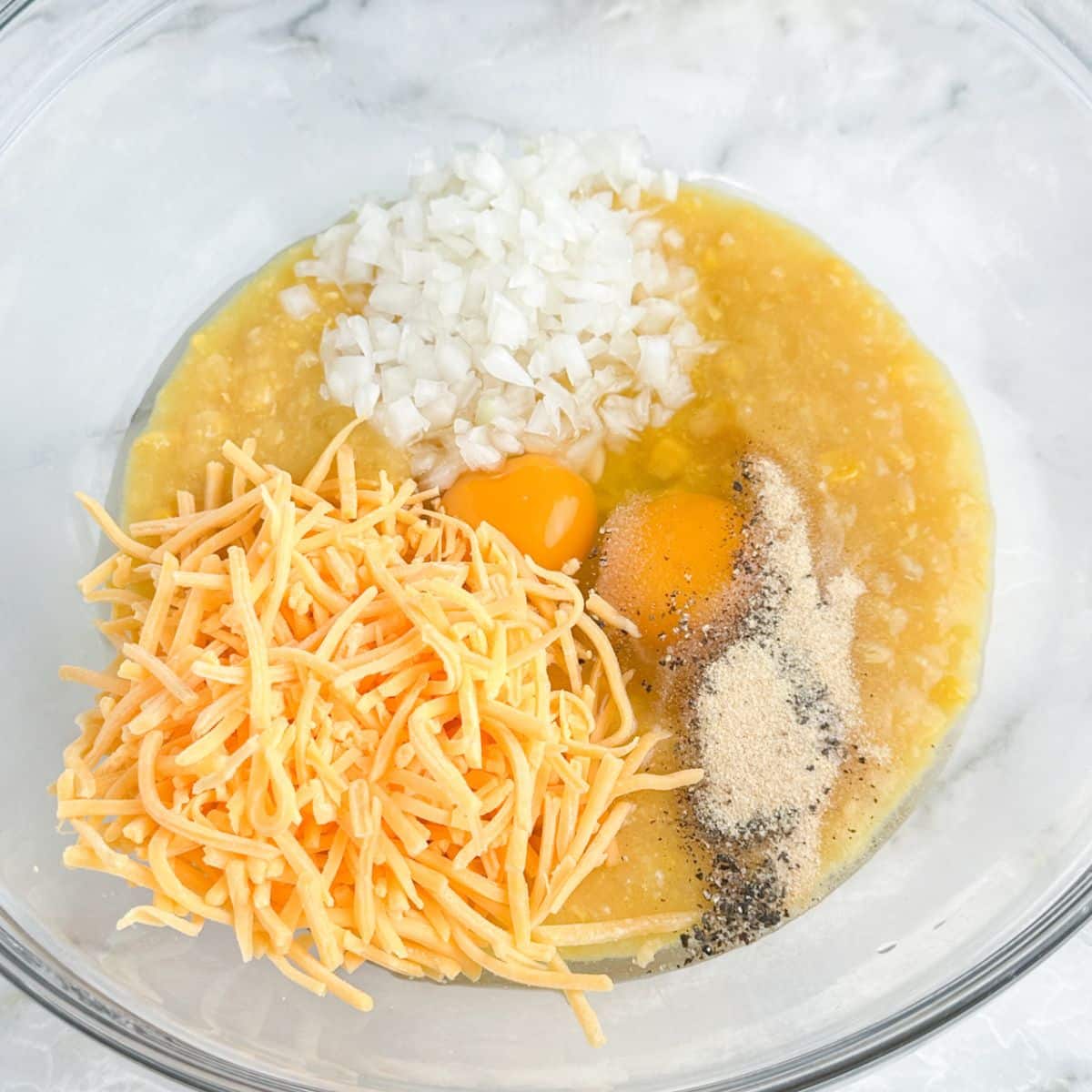 Bowl of creamed corn, eggs, shredded cheese, and diced onions. 