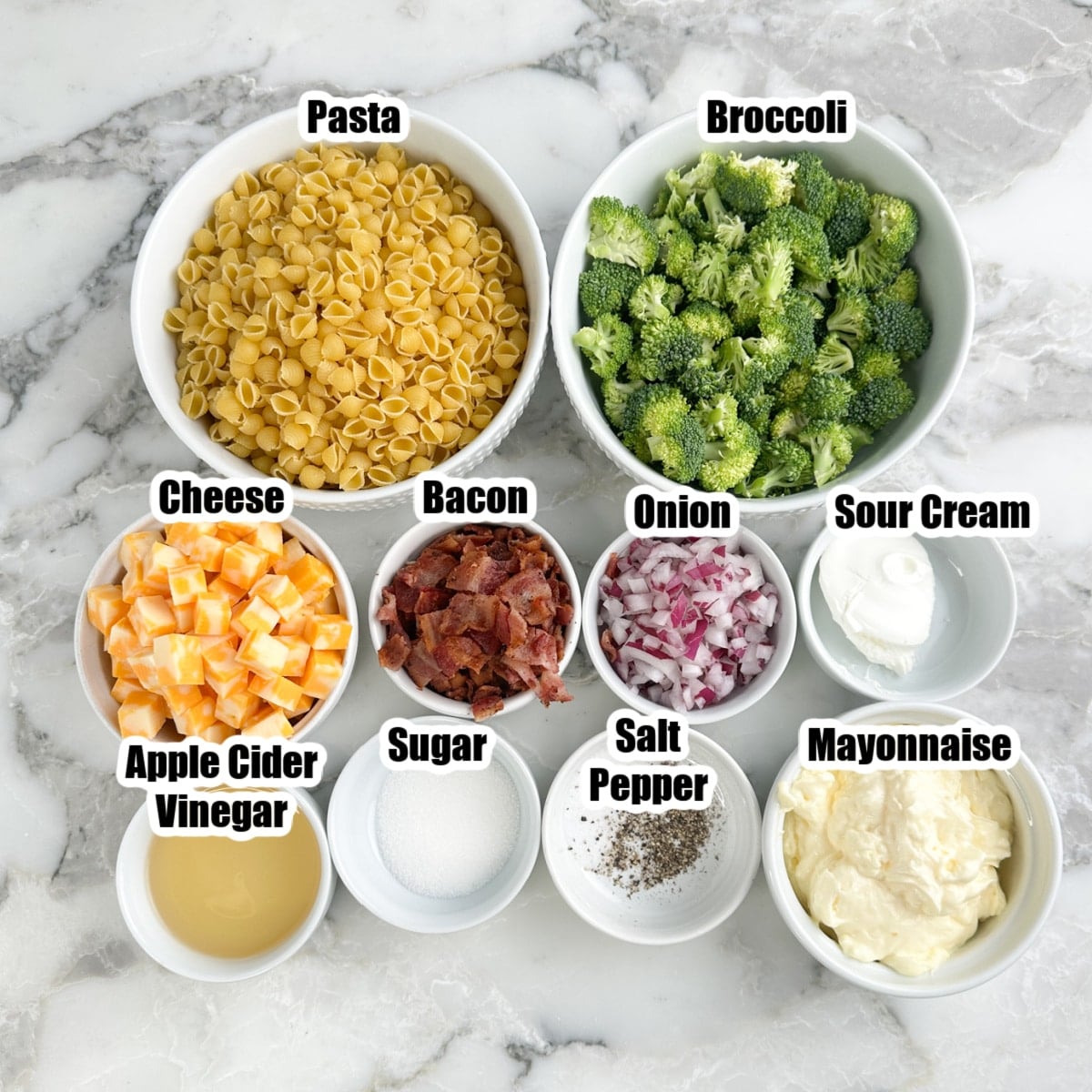 Bowl of pasta, broccoli, cubed cheese, bacon, onions, sour cream, mayonnaise, vinegar, sugar, salt, and pepper. 
