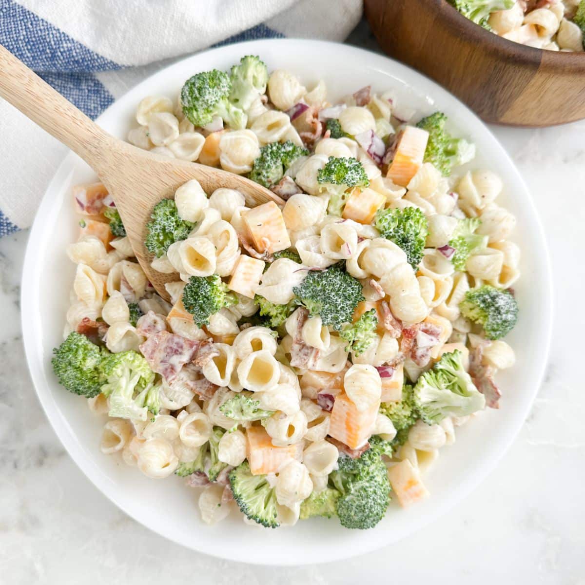 Bowl of broccoli pasta salad with a wooden spoon. 