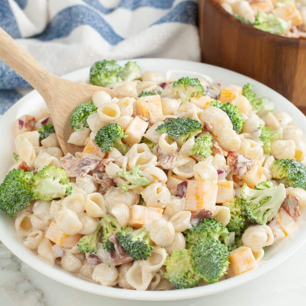 Bowl filled with broccoli pasta salad and wooden spoon. 