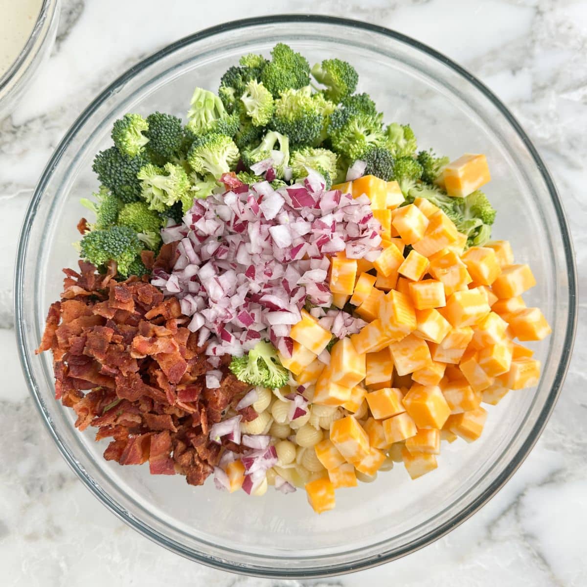 Bowl with pasta, bacon, broccoli, cheese, and red onion. 