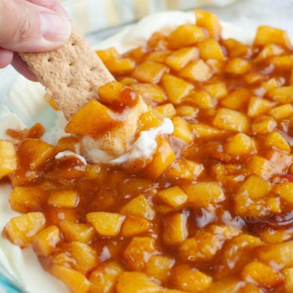 Hand dipping a graham cracker in peach pie dip.