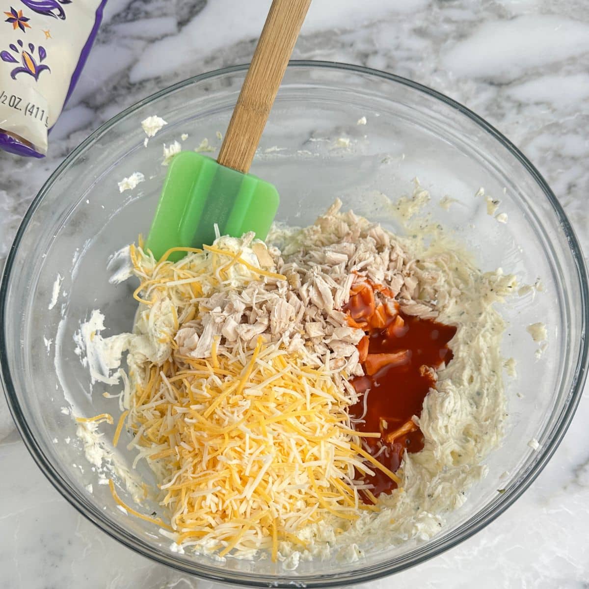 Bowl with cream cheese, shredded cheese, chicken, and buffalo sauce.