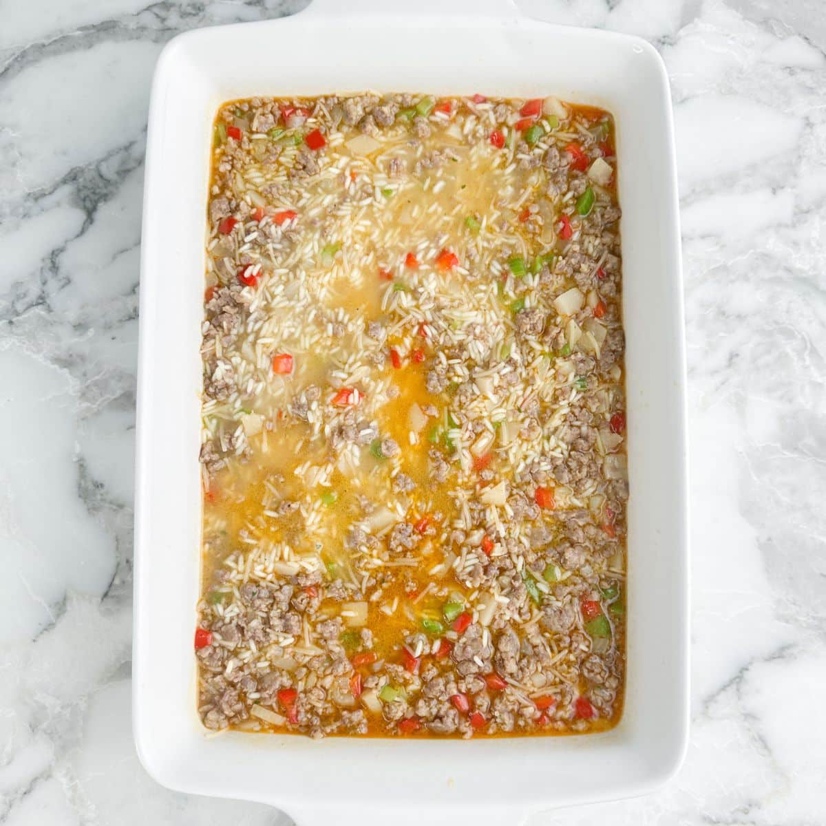 Casserole dish with unbaked sausage and rice casserole.