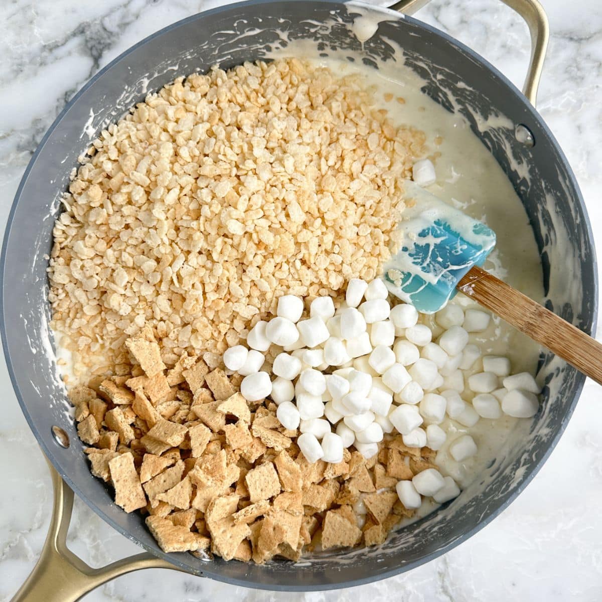 Large skillet with melted marshmallows, rice krispies, mini marshmallows, and broken graham crackers.