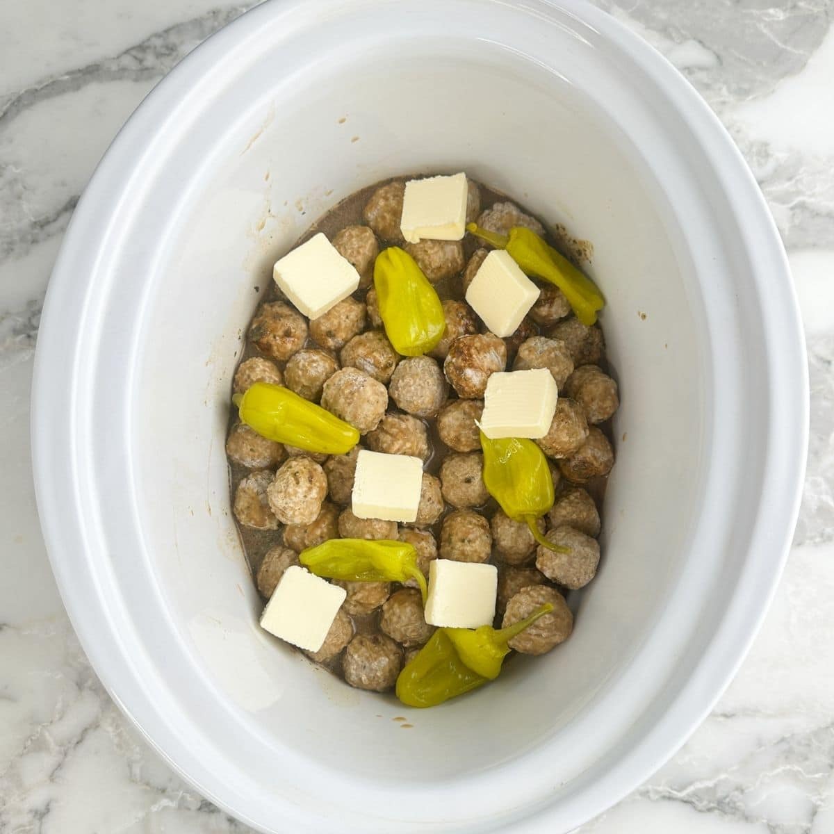 Slow cooker with meatballs, butter, and pepperoncinis.