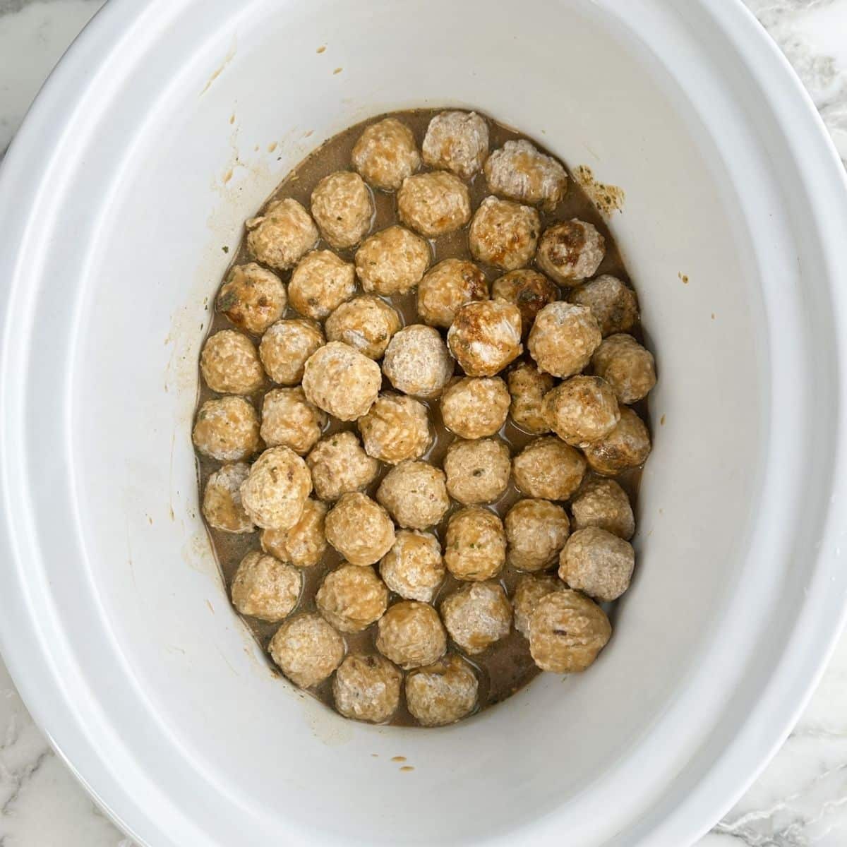 Slow cooker with frozen meatballs and sauce.
