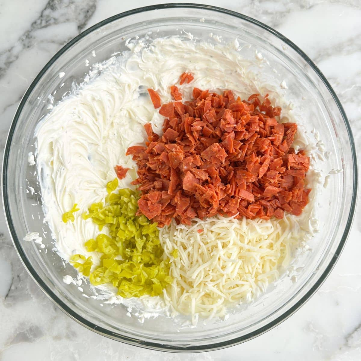 Bowl with whipped cream cheese, chopped pepperoni, mozzarella cheese, and chopped peperoncini peppers. 