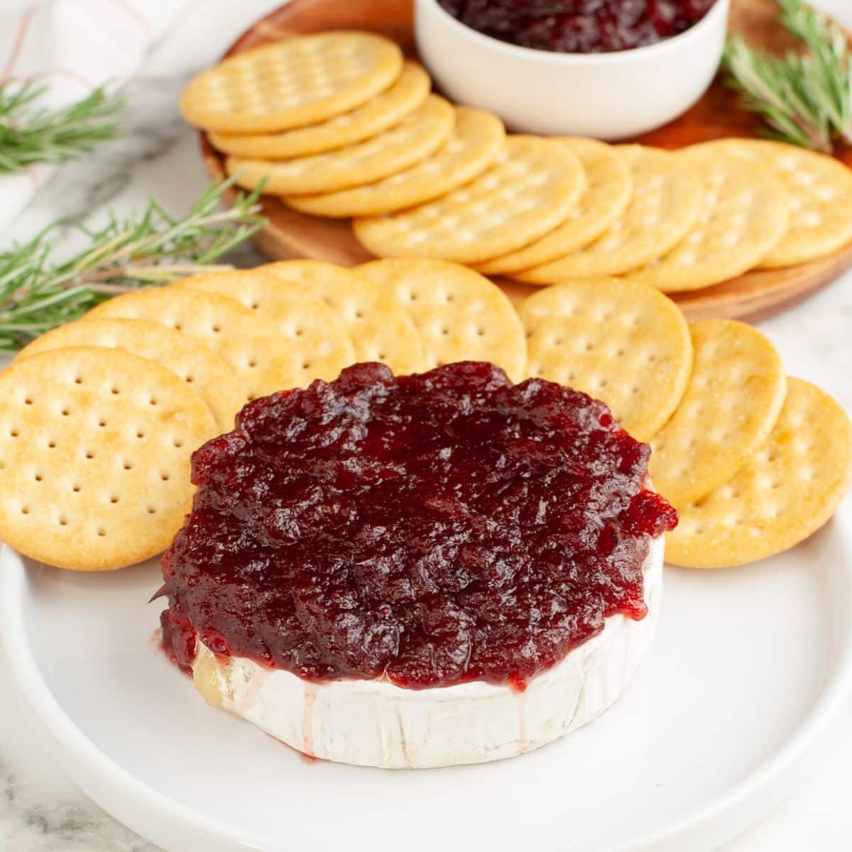 Plate with baked brie topped with cranberry sauce and crackers.