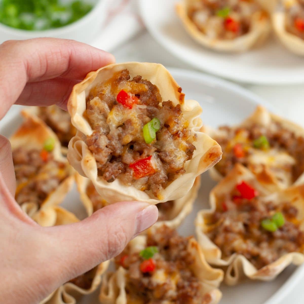 Hand holding a cheesy sausage wonton cup.