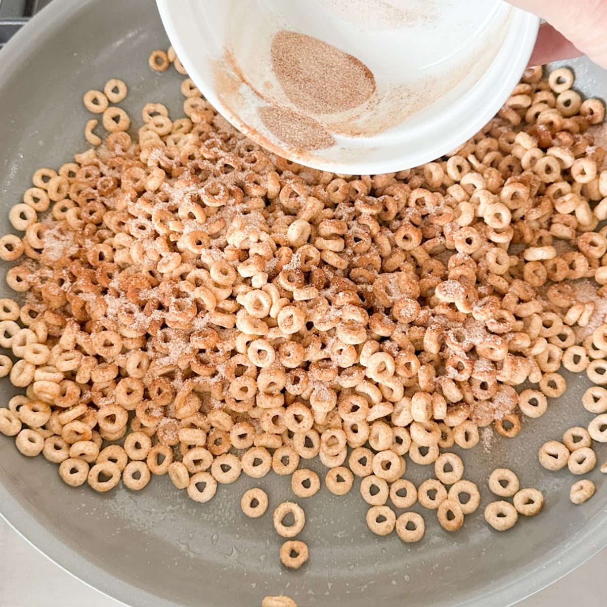 Skillet with Cheerios with cinnamon and sugar being sprinkled on. 