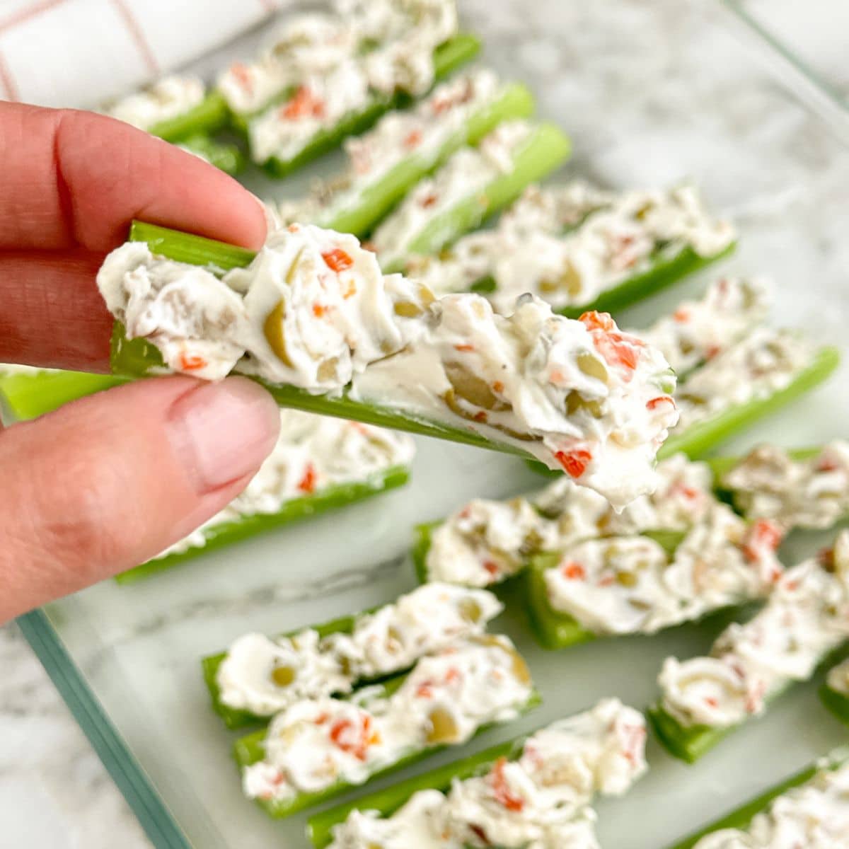 Hand holding a piece of celery stuffed with cream cheese and olives. 