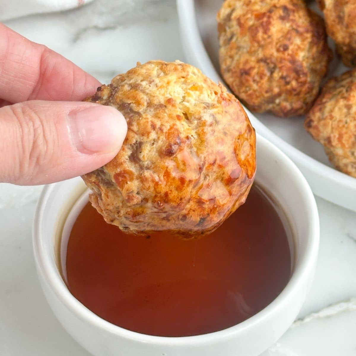 Hand holding a pancake mix sausage ball dipping in syrup.