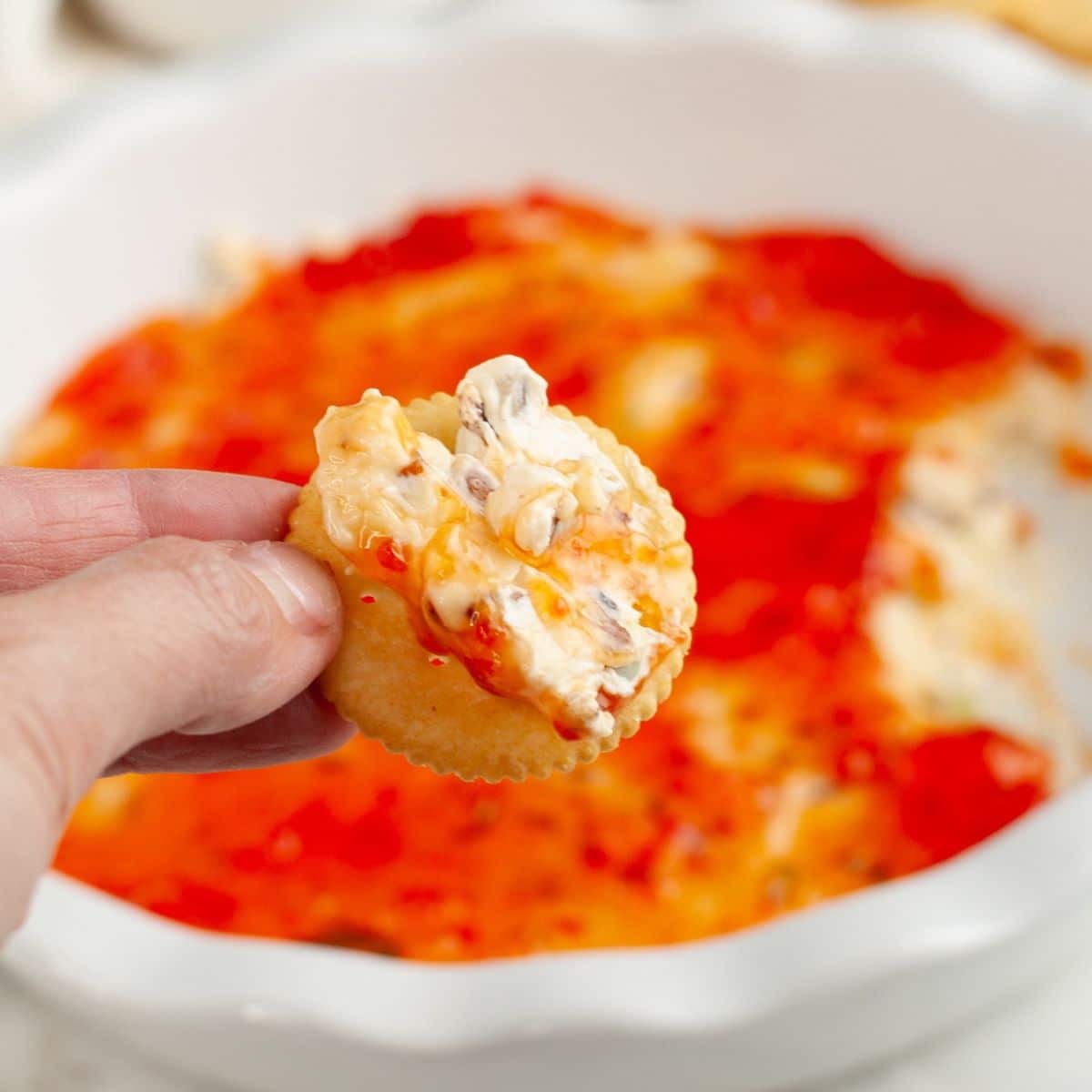 Hand holding a cracker with pepper jelly dip.